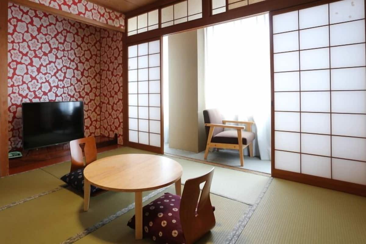 A traditional Japanese room with tatami flooring, a low table, a television, and sliding doors.