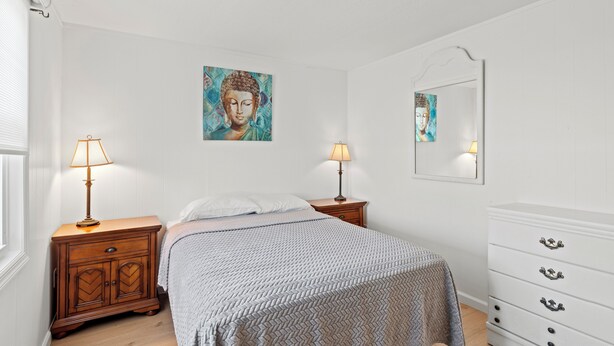 Ein Schlafzimmer mit einem Bett, zwei Nachttischen mit Lampen, einer Kommode und einem an der Wand befestigten Spiegel.
