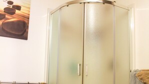 A bathroom with a glass shower enclosure, a towel rack with towels, and a wall-mounted towel rack.