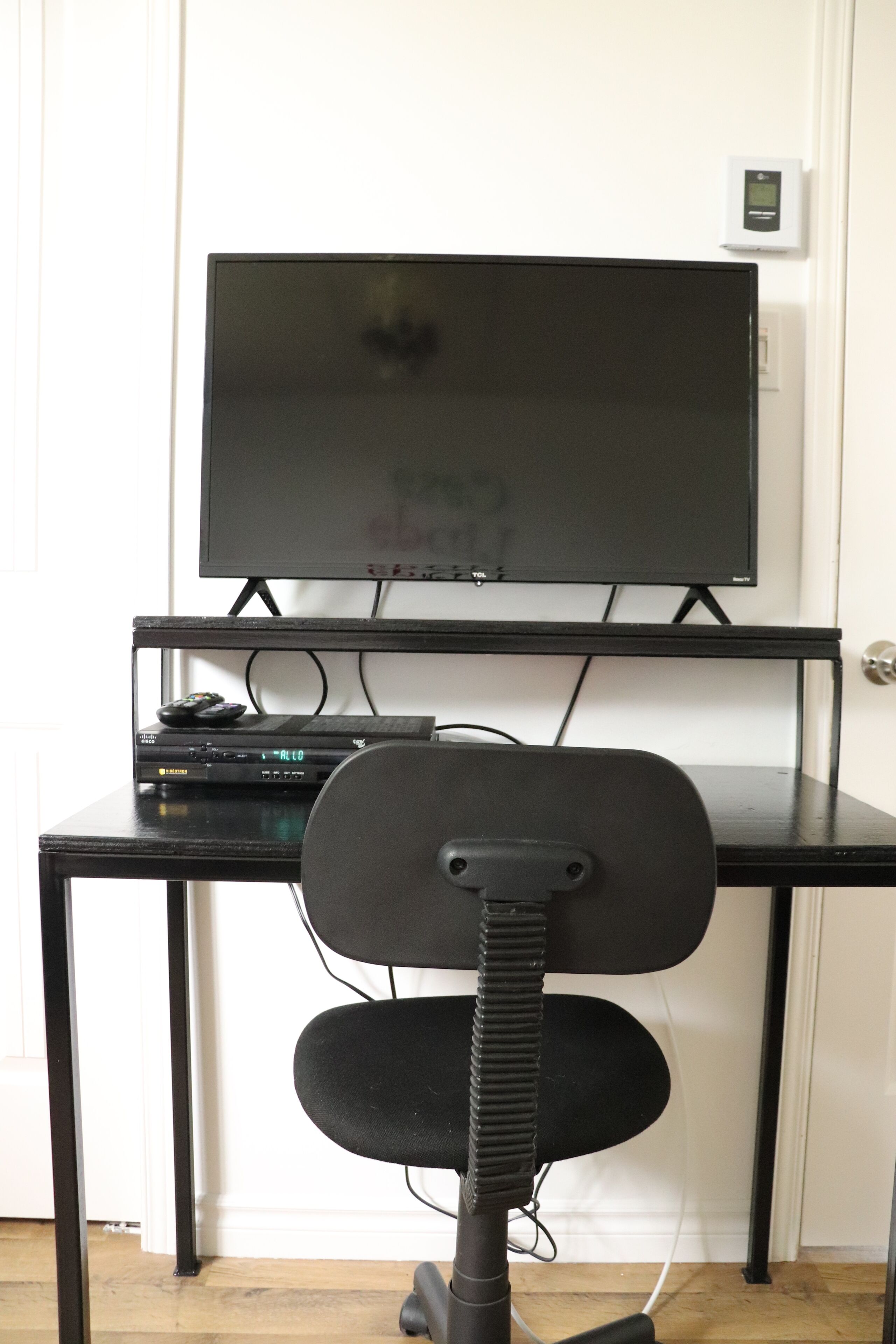 A black office chair with a headrest and a desk with a flat-screen TV mounted on it.