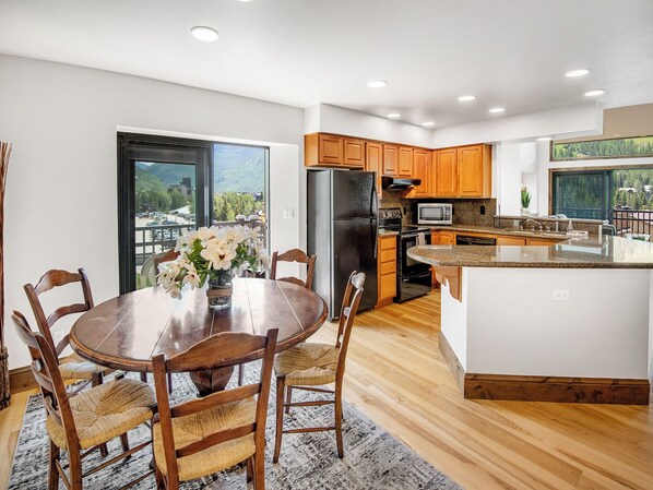 A modern kitchen with wooden cabinets, a central island, and a dining area with a table and chairs. - Vantage Point Condo 502 | 2BR + Loft in Lionshead Village (Vail)