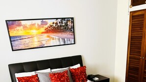 Un lit bien fait, agrémenté d’une décoration réalisée avec des serviettes, une table de chevet, un téléphone et un tableau représentant un coucher de soleil accroché au mur.