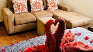 Une pièce comprenant un canapé et un lit, avec des serviettes rouges et des pétales de rose.