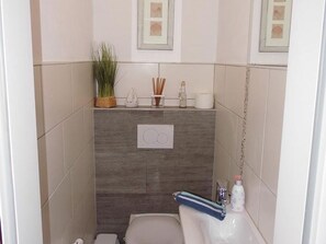 A small bathroom with a toilet, a sink, and a shower. There are framed pictures on the wall, a plant, and a towel hanging on the sink. - Ferienhaus Mühlenblick 41 Nr. 2 (Wittmund)