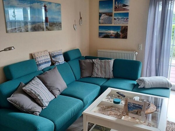 Ein hölzernes Sofa in Petrolfarbe mit gestreiften Kissen, ein weißer Couchtisch mit Dekoration und eine Wand mit gerahmten Bildern.