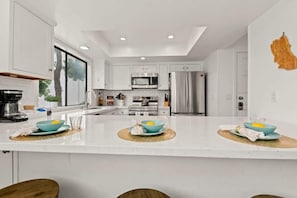 A modern kitchen with white cabinets, stainless steel appliances, and a central island with blue bowls.