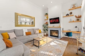 A modern living room with a grey sofa, a coffee table, a fireplace, and a Netflix sign.