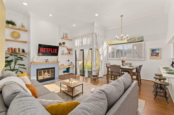 A modern living room with a fireplace, a dining area, and a kitchen.