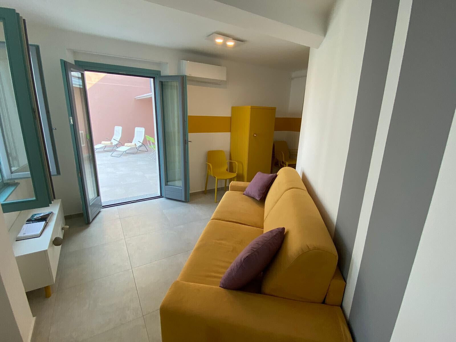 Ein modernes Hotelzimmer mit einem gelben Sofa, einem kleinen Tisch und einer Schiebetür zu einem Sitzbereich im Freien.