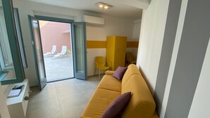 A modern hotel room with a yellow sofa, a small table, and a sliding glass door leading to an outdoor seating area. - Stone apartment with lake view in Baveno (Baveno)