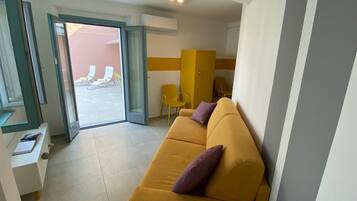 Ein modernes Hotelzimmer mit einem gelben Sofa, einem kleinen Tisch und einer Schiebetür zu einem Sitzbereich im Freien.