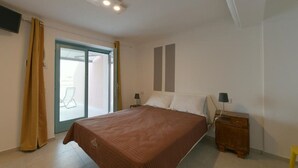 A bedroom with a bed, two bedside tables, a sliding glass door, and a small table with a chair outside. - Stone apartment with lake view in Baveno (Baveno)