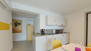 A compact kitchen with white cabinets, a microwave, and a coffee maker. There is a dining area with a table and chairs, and a yellow door in the background. - Stone apartment with lake view in Baveno (Baveno)