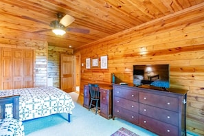 Habitación con paneles de madera, una cama, cómoda, televisor y ventilador de techo.