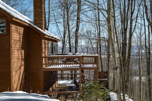Una cabaña de madera con un balcón que da a un bosque nevado.