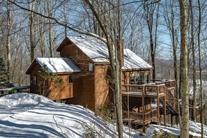 A wooden cabin with a balcony, surrounded by trees and snow.