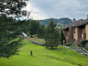 A residential area with a wooden staircase leading to a house, surrounded by lush greenery and a mountain in the background.