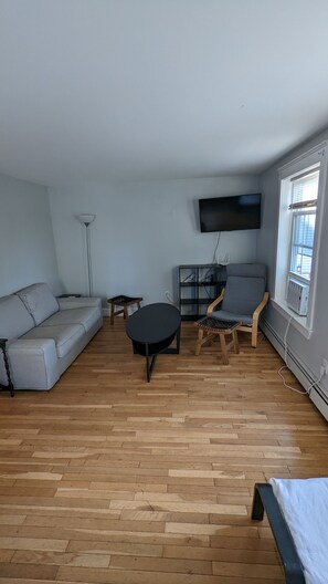Un salon avec un canapé, une table basse, un fauteuil, un téléviseur et une fenêtre.