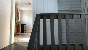 Una escalera de madera con barandilla negra que lleva a una habitación con paredes y puerta blancos.