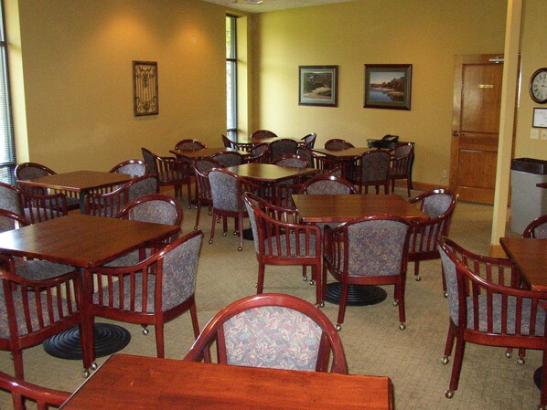 A dining area with multiple wooden tables and chairs, framed pictures on the walls, and a clock on the right.