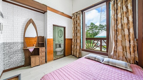 Un dormitorio con un ventanal grande, muebles de madera, una cama con ropa de cama rosa y vistas a zonas verdes.