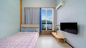 Un dormitorio con cama, televisor, banco y ventana con vistas a montañas.