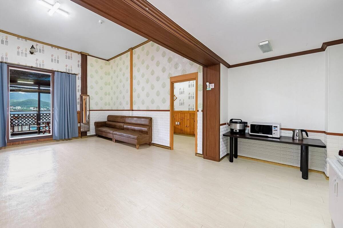 Un salón amplio con sofá, zona de cocina con microondas y tetera, y balcón con vistas.
