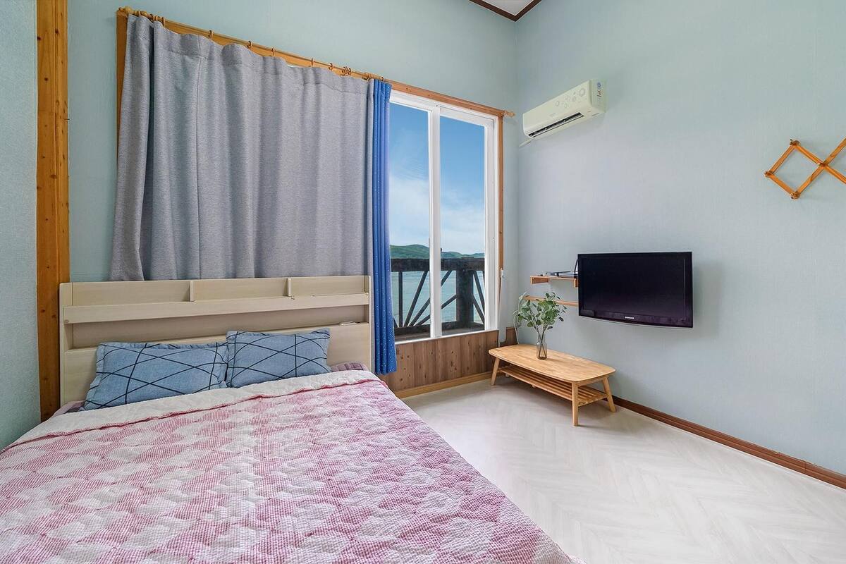 Un dormitorio con cama, televisión, ventana con cortinas y vistas al exterior.