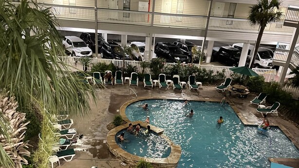Una piscina interior con varios niveles de balcones, rodeada de sillones de descanso y palmeras.