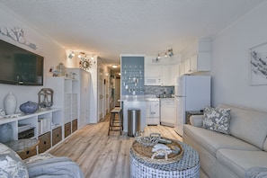 Un espacio habitable compacto con kitchenette, un sofá, un televisor y elementos decorativos.