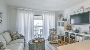 Una sala de estar con sofá, sillón y reposapiés, televisión y estantería.