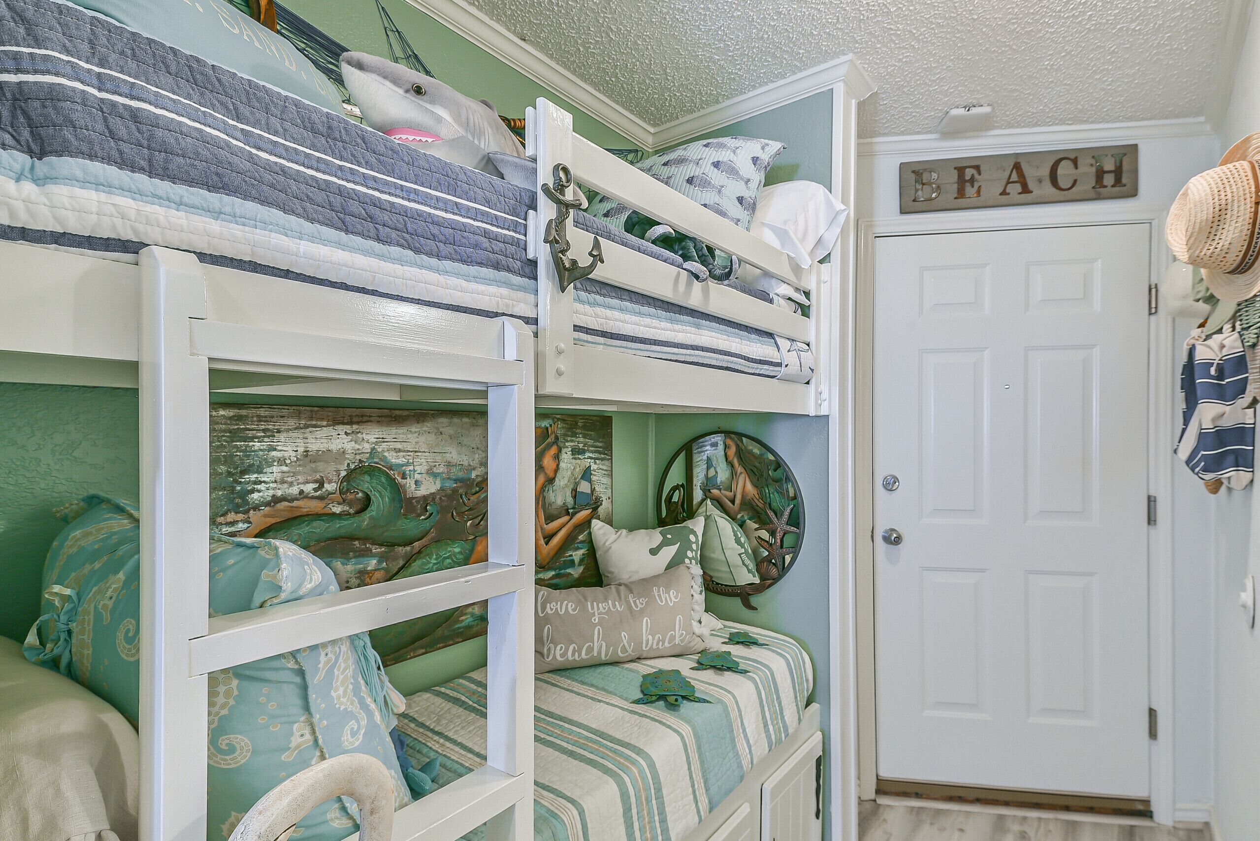 A bunk bed with nautical-themed bedding and a door with a 'BEACH' sign.