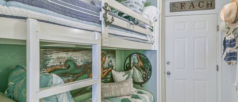 A bunk bed with nautical-themed bedding and a door with a 'BEACH' sign.
