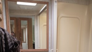 Une salle de bain équipée de toilettes, d’une douche, d’un miroir et d’un porte-serviettes.