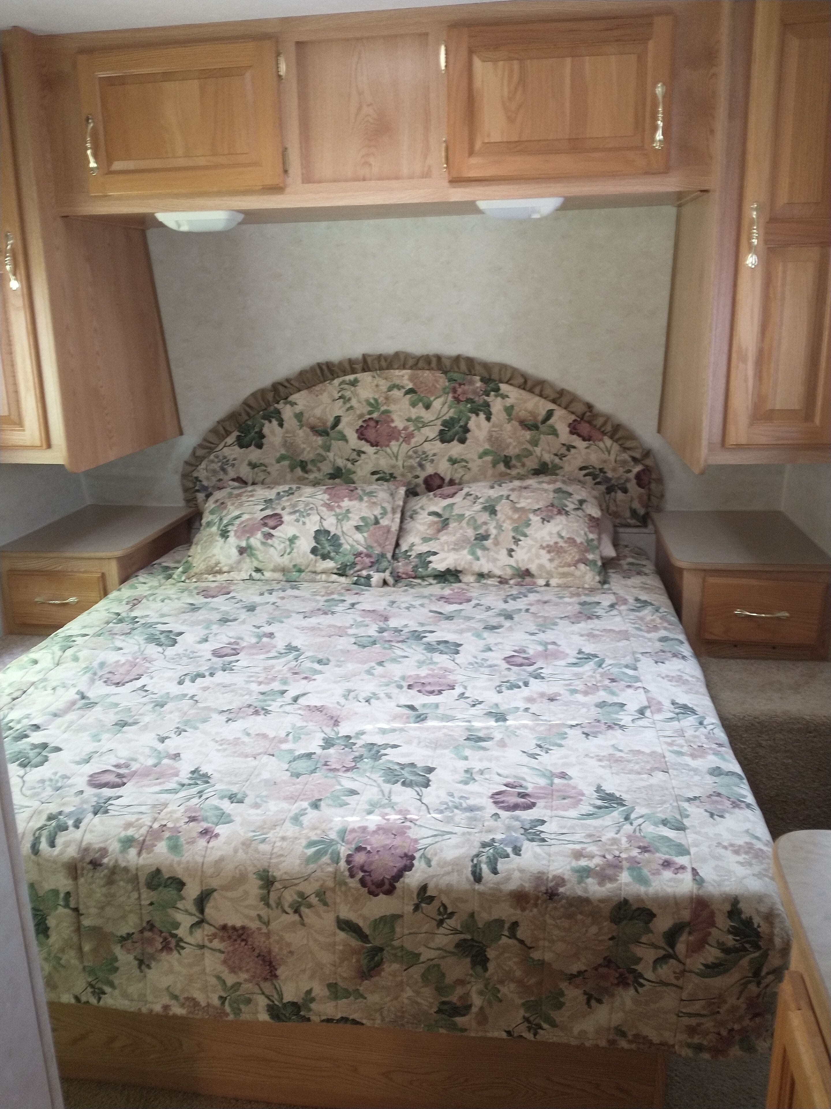 A bedroom with a floral bedspread, wooden headboard, and built-in wooden cabinets above the bed.