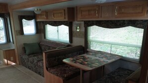 Un intérieur de camping-car compact comprenant un coin repas, des sièges et une fenêtre avec des stores.