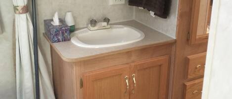 A small bathroom with a wooden vanity, a sink, and a mirror. There is a towel hanging on the wall and a tissue box on the counter.