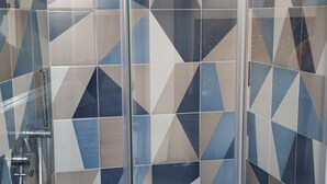 Una ducha con puerta de cristal, diseño de azulejos geométrico y un cabezal de ducha de mano.