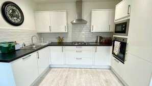 A modern kitchen with white cabinets, a black countertop, stainless steel appliances, and a clock on the wall.