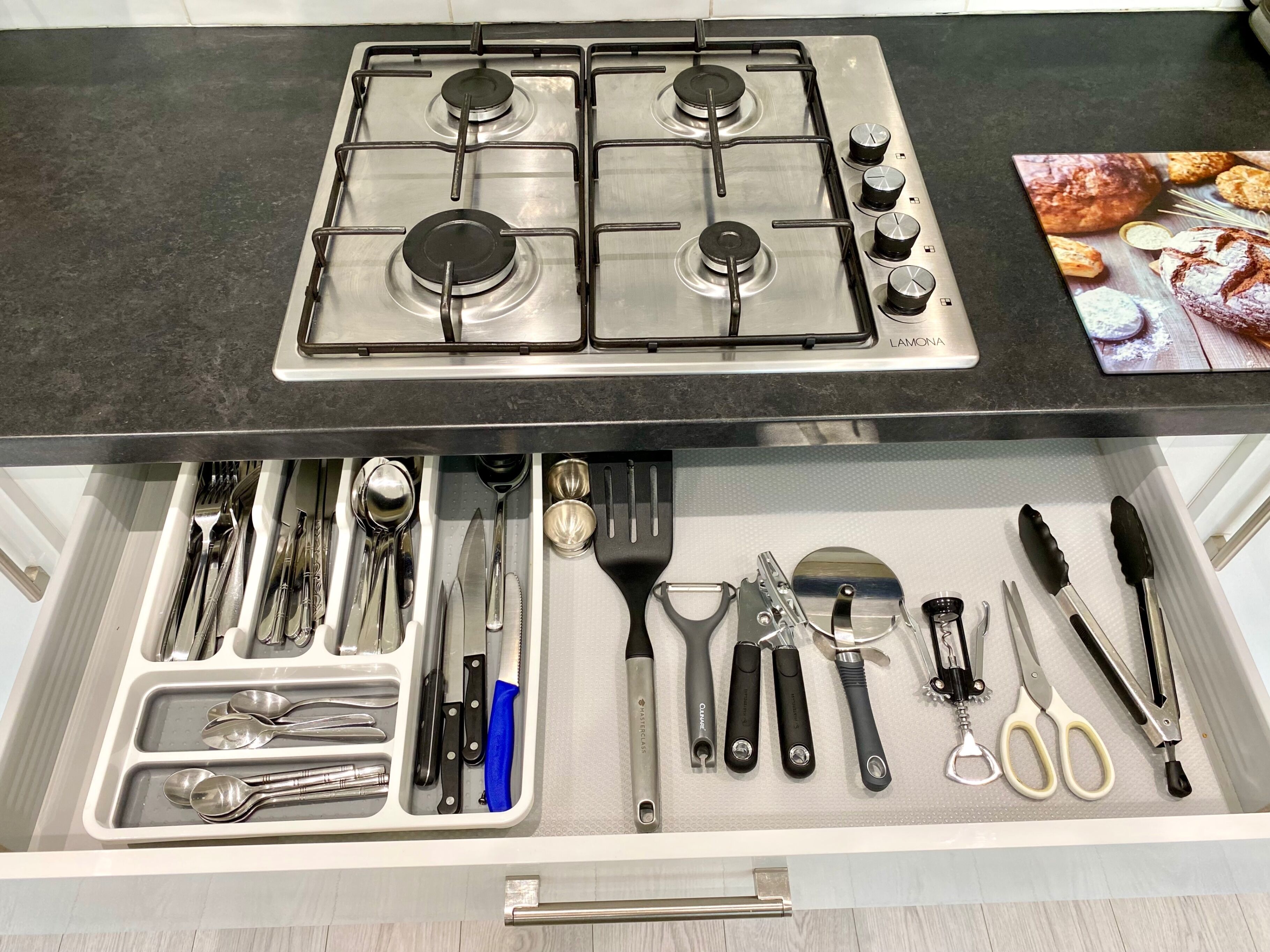 A kitchen with a stove and a drawer containing utensils.