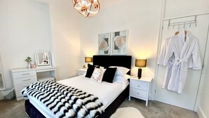 A bedroom with a bed, bedside tables, a mirror, a hanging robe rack, and a chandelier.