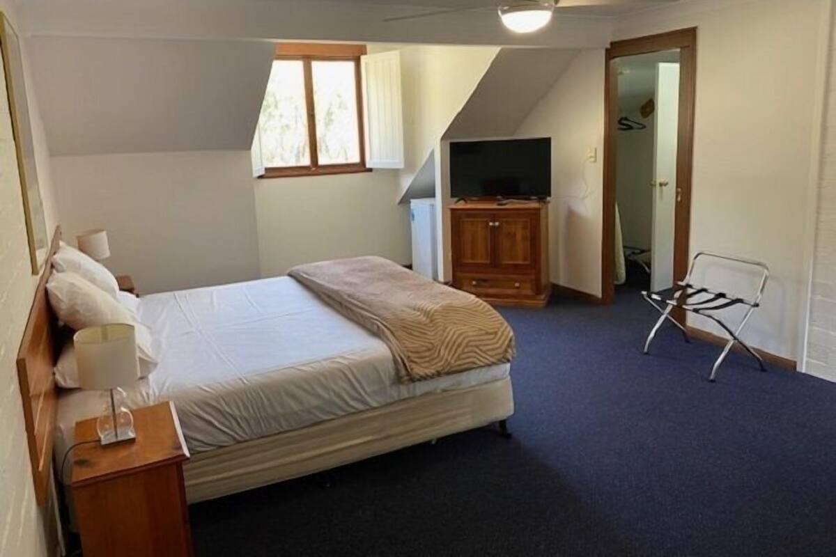 Un dormitorio con cama, mesita de noche, lámpara, mueble para televisor y una silla.