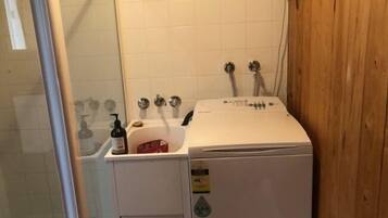 A compact, white laundry room with a washing machine, a small sink, and a shower area.