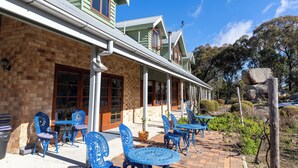 A brick building with a green facade, a covered patio with blue metal chairs and tables, and a garden with rocks and shrubs. - Girraween Country Inn (Eukey)