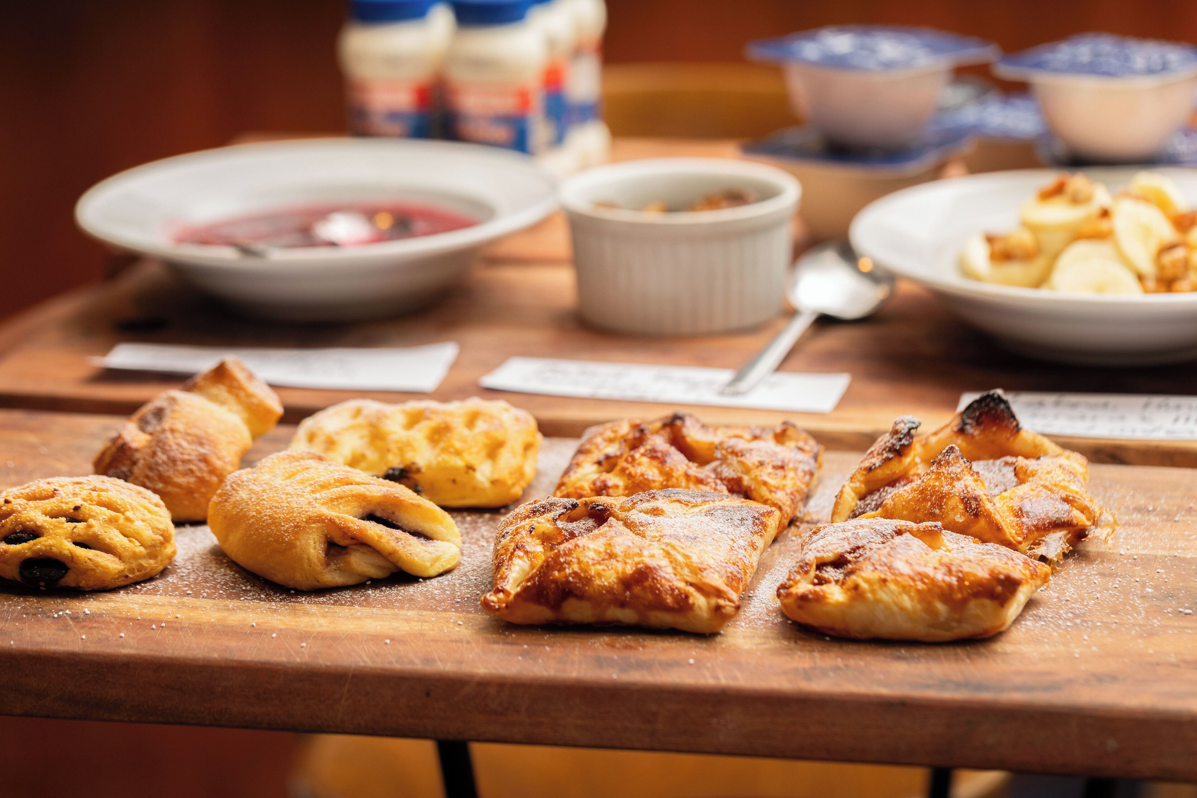 A wooden table with pastries and bowls of food.