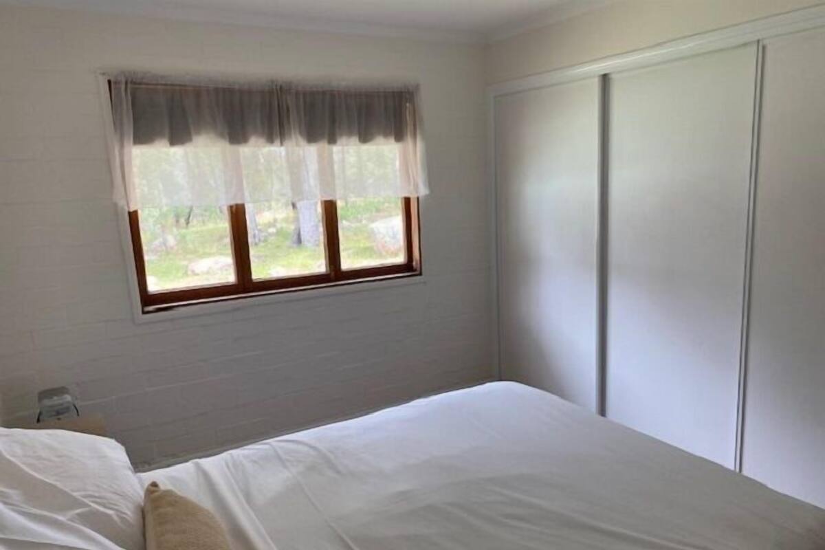 Un dormitorio con cama, ventana con cortinas y armario.