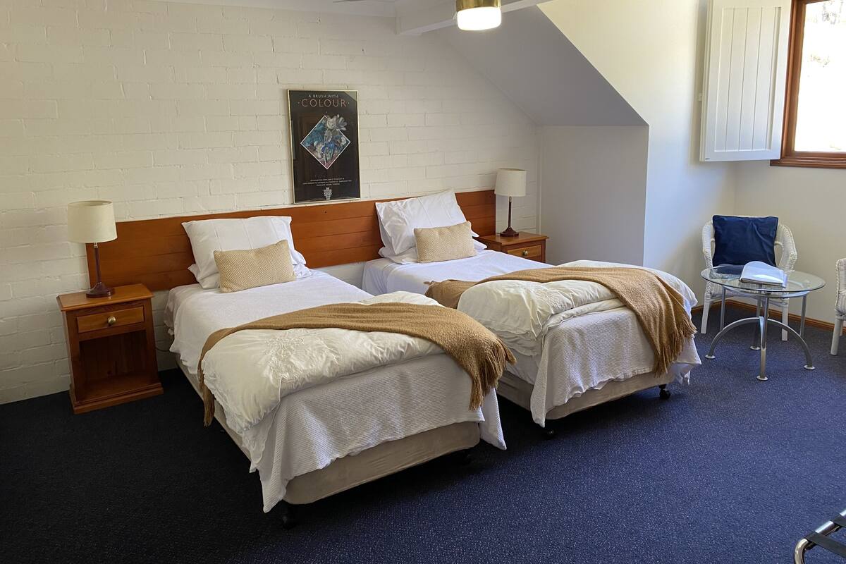 Una cama doble con cabecera de madera, dos mesitas de noche con lámparas, una pequeña mesa redonda con una silla y un ventilador de techo.