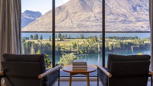 A room with a large window offering a view of a lake and mountains. There are two chairs and a small table in the room. - Fernlea by MajorDomo | Beautifully Renovated Home with Dramatic Lake Views, Spa Pool & Wrap-Around Veranda, Walk to Town (Queenstown)