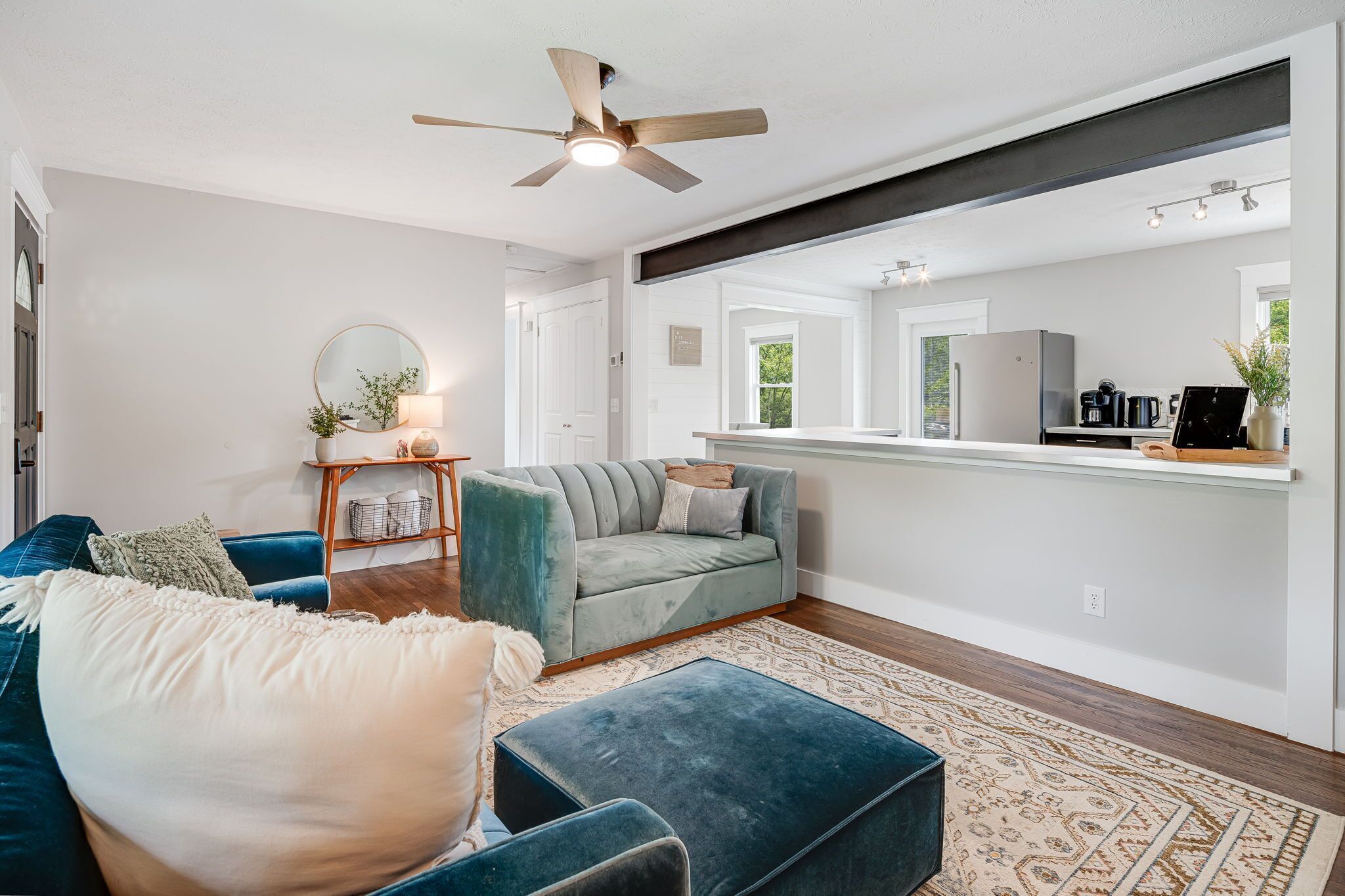 A modern living room with a grey sofa, blue ottoman, and a ceiling fan.