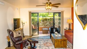 A living room with a leather recliner, a wooden coffee table, a red sofa, a ceiling fan, and a large sliding glass door leading to an outdoor area. - Eclectic boho style apartment in the heart of West Sedona (Sedona)